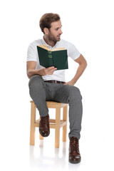 man sitting holds a book and looks to side