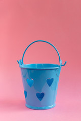 Decorative blue bucket with heart shaped holes on pink background. Festive concept.