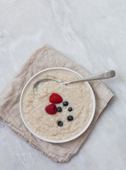 Oatmeal porridge with fresh berries on marble background