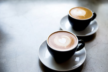 Two black cups of tasty cappucino with love art latte.