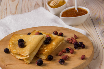 Pancakes on a wooden board with honey, jam and berries