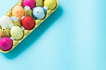 Easter eggs are painted in bright colors, lie in a cardboard eco-packaging. Blue background. Easter...
