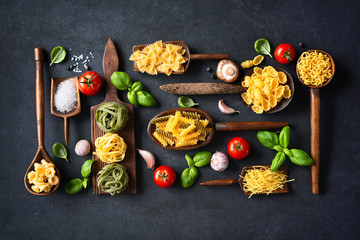 Various pasta on wooden spoons over stone background