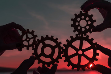 Four gears in the hands of people against the evening sky. Teamwork, interaction.