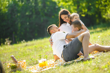 Fototapeta premium Young family having picnic outdoor. Mother, father and their kids having fun in the park. Summer resting at the nature.
