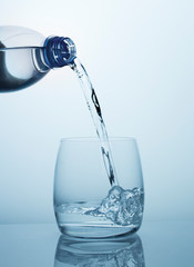 Clean drinking water flows from the bottle into a clear glass with beautiful bubbles.