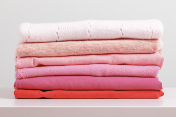On a pink dresser is a stack of folded clothes. Gray background. Close-up