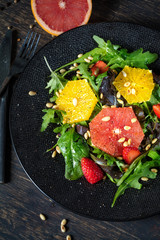 Grapefruit and orange mix salad with pine nuts on black plate and dark background, vertical composition