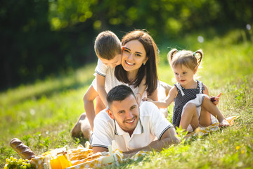 Young family having picnic outdoor. Mother, father and their kids having fun in the park. Summer resting at the nature.