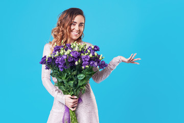 Young happy smiling redhead woman holding bouquet of violet spring flowers isolated on blue background. Festive bouquet in honor of women's day on March 8 or birthday