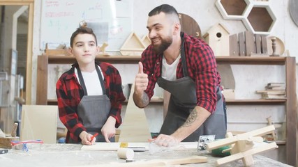 Father and little son giving high five while visiting woodworking masterclass at workshop