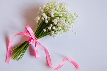Close-up bouquet of lilies of the valley tied with a pink ribbon on white background. Place for...