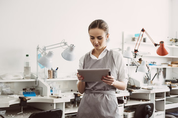 Online business. Close up portrait of young female jeweler in apron holding digital tablet.