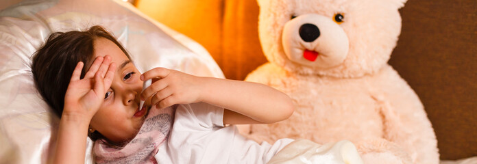 Sick girl lying in bed with a thermometer in mouth and touch his forehead