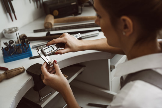 High precision. Close up photo of a young female jeweler measuring ring with a tool in workshop. - Powered by Adobe