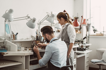 Master and apprentice. Young male assistant and female jeweler are working together at jewelry...