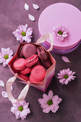 Pink and purple macaroon close-up in a gift paper bag on a purple background decorated with flowers. Top view, selective focus. March 8, Women's Day.