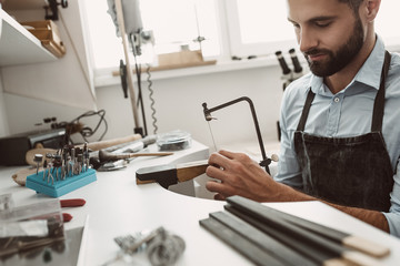 Perfect working day. Portrait of male jeweler making a silver ring with professional adjustable...