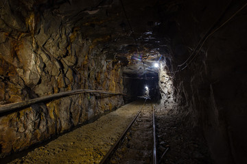 Naklejka premium Underground gold ore mine shaft tunnel gallery passage with rails and light