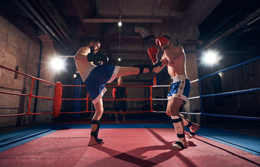 Two handsome men boxers exercising kickboxing in the ring at the sport club