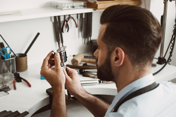 Exact size. Close up photo of a young male jeweler measuring ring with a tool in workshop.