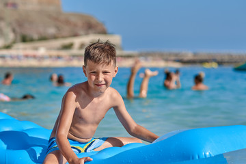 Good-looking European boy is sitting on the inflatable matress in the sea and smiling to the camera.
