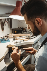 Made with love. Vertical photo of young male jeweler working and shaping an unfinished ring with a...