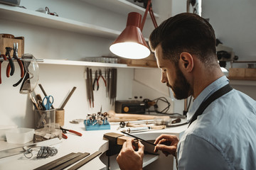 A lot of work in the workshop. Close up of a young male jeweler working and shaping an unfinished ring with a tool in workshop