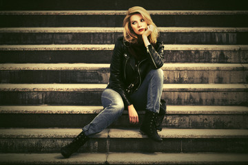 Young fashion blond woman in leather jacket sitting on steps