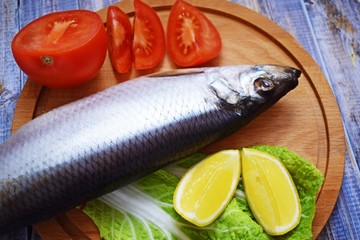 Delicious herring with lemon and tomatoes on lettuce leaves.