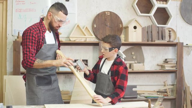 Father and little son testing hand-made wood sword evenness at workshop.