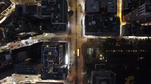 Drone shot looking down at the pedestrian crosswalk in downtown Hong Kong at night.