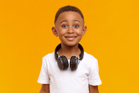 Positive human facial expressions, emotions and reaction. Isolated image of emotional handsome black schoolboy wearing white top and wireless headset around his neck, being amazed or excited