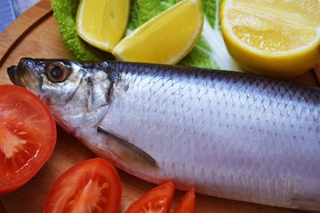 Delicious herring with lemon and tomatoes on lettuce leaves.