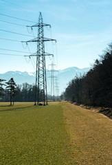 high voltage power lines and tall lattice crosses in rural countryside with snow-capped mountain peaks in the background