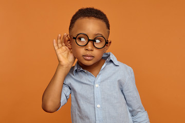 I want to hear everything. Handsome nosy African American little boy wearing round spectacles and...
