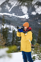 The photographer with camera on the cliff in winter mountains