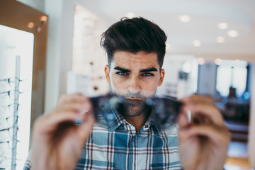 Handsome young man choosing eyeglasses frame in optical store.