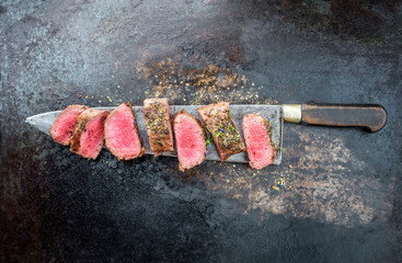 Traditional barbecue aged venison backstrap roast sliced with herbs as top view on a large knife...
