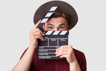 Caucasian successful male producer looks through oprnrd clapperboard, works on film production,...