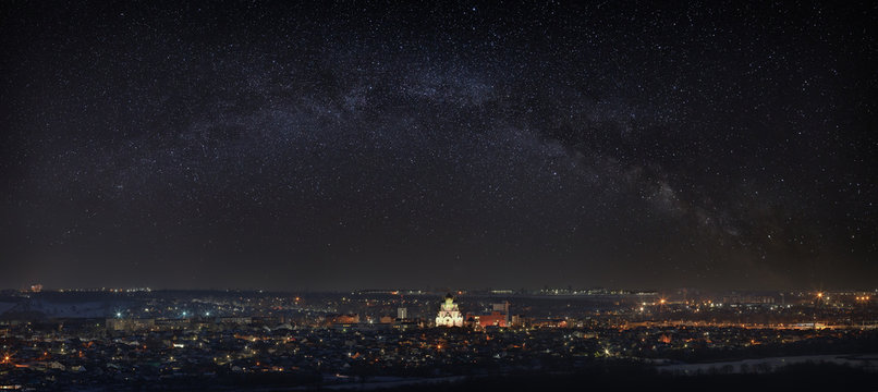 Milky Way over the city. Bright stars in the night sky. The streets are lit by lanterns. Panoramic view of the Orthodox Church.