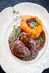 Traditionelle geschmorte Schweinebäckchen  in brauner Rotwein Sauce mit Pilzen und Kürbis als closeup auf einem weißen Shabby Chic Design Teller