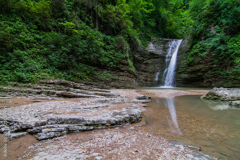 Wall mural high waterfall flowing down the wall in the forest on a cloudy day