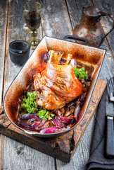 Traditionelle gegrillte bayrische Schweinshaxe mit Zwiebel als closeup in einem rustikalen Schmortopf auf einem alten Holz Board