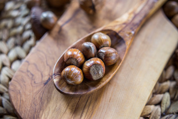 Shelled whole hazelnuts on a wooden spoon over a cheese board with mixed nuts in background