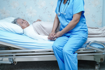 Obraz premium Asian nurse physiotherapist doctor care, help and support senior or elderly old lady woman patient lie down in bed at hospital ward : healthy strong medical concept.