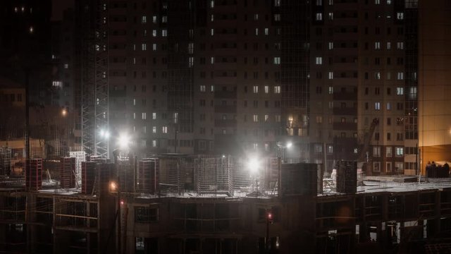 Construction site residential housing estate building in the city, building constructors working at winter night in bad weather conditions snowing, crane in time lapse
