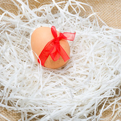 Brown Easter eggs tied with a red satin ribbon lay in the wood shavings on the linen burlap.Holiday greetings.