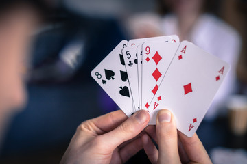 Friends are playing cards together at home. Man is holding cards in her hands, woman in the blurry...