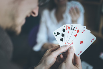 Friends are playing cards together at home. Man is holding cards in her hands, woman in the blurry background.